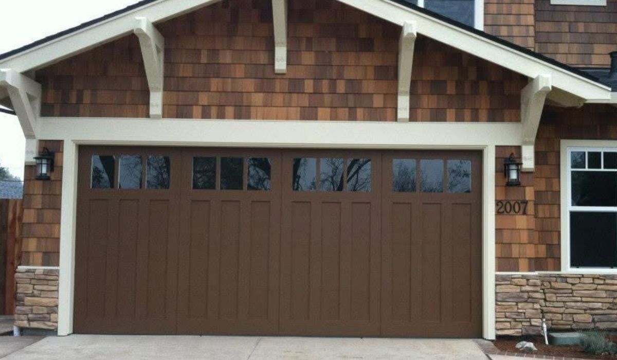 Brown double garage door on a house exterior with stone siding and white trim