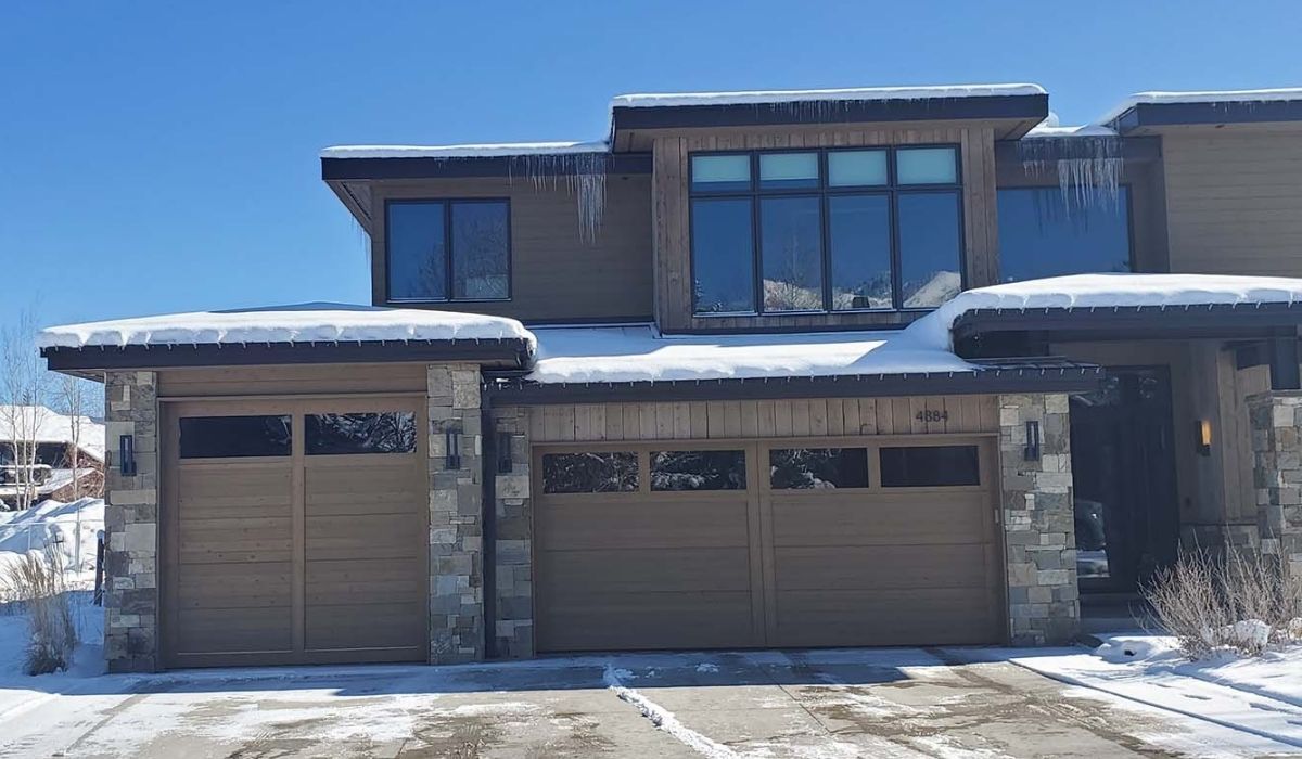 Snow-covered modern two-story house with three garage doors on a sunny day