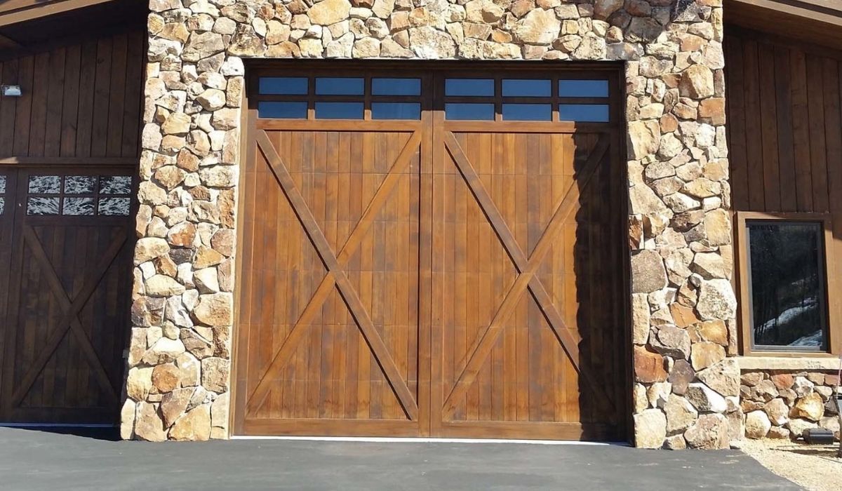 Wooden double garage door set in a stone wall with narrow windows above and on the side
