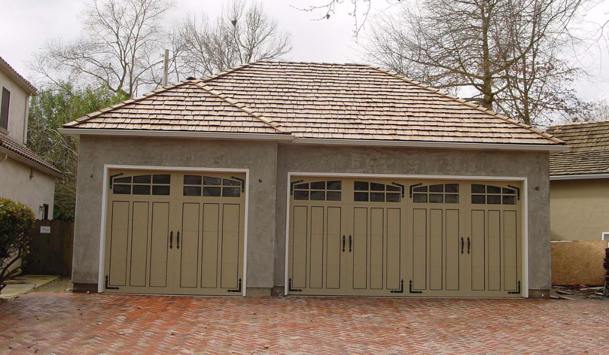 Two-car garage with beige doors and a brown shingle roof, set in a brick-paved driveway