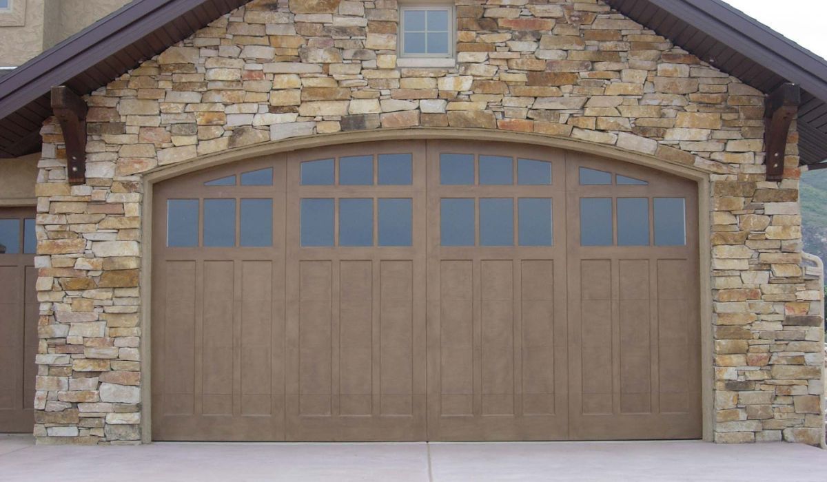 Stone house front with a brown double garage door and arched windows
