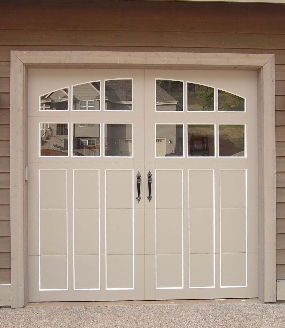 White double garage doors with small window panes and black handles on a beige house.