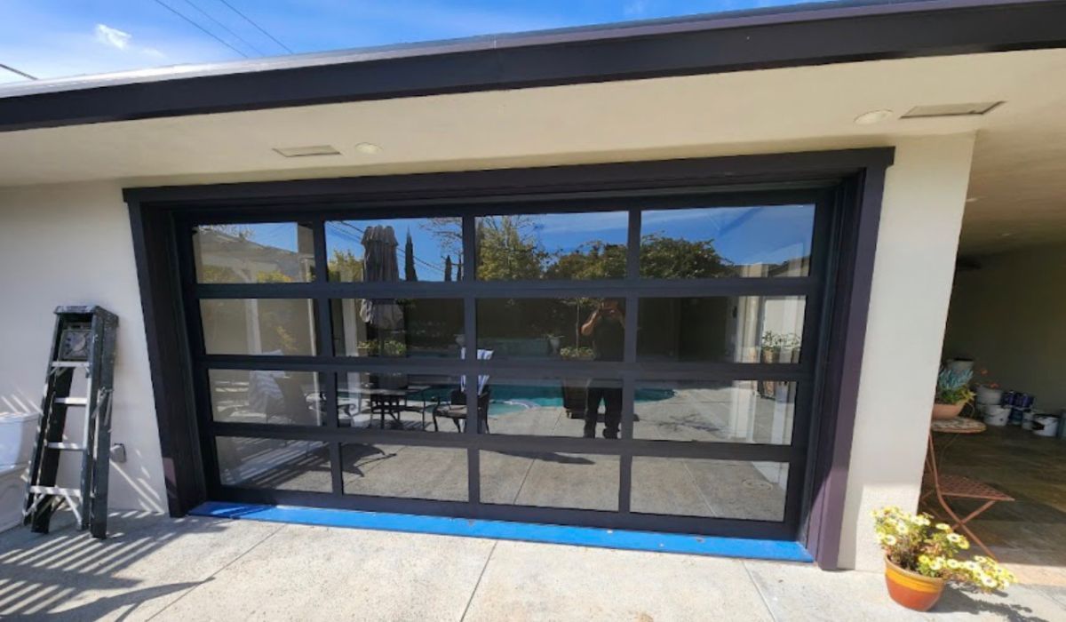 Modern black-framed sliding glass doors on a white house patio, with a ladder and potted plant nearby