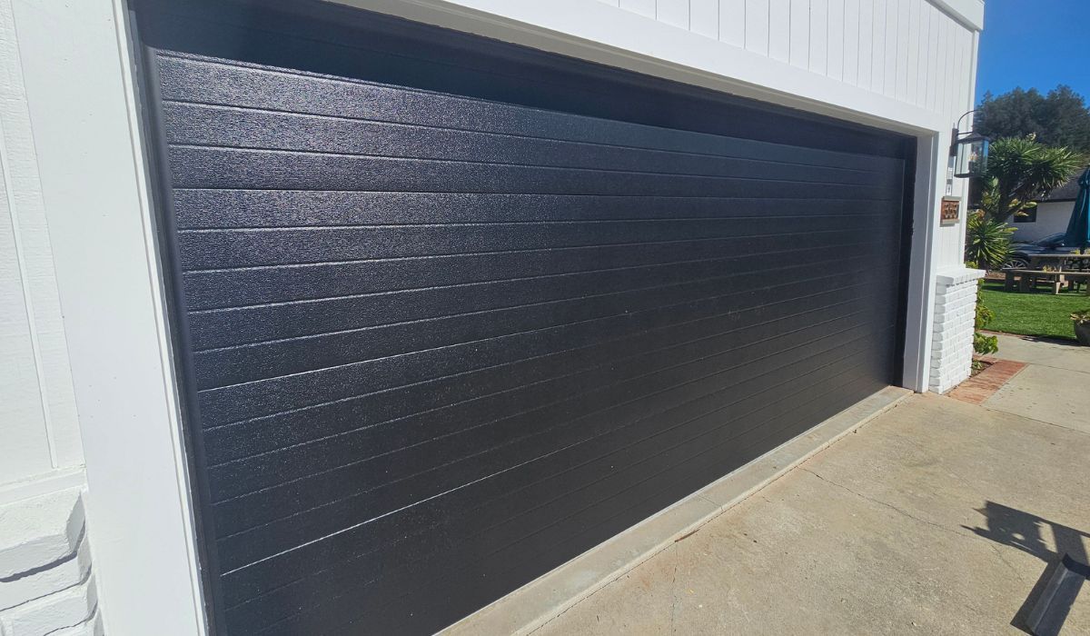 Black sectional garage door on a white building, viewed from the driveway in bright sunlight