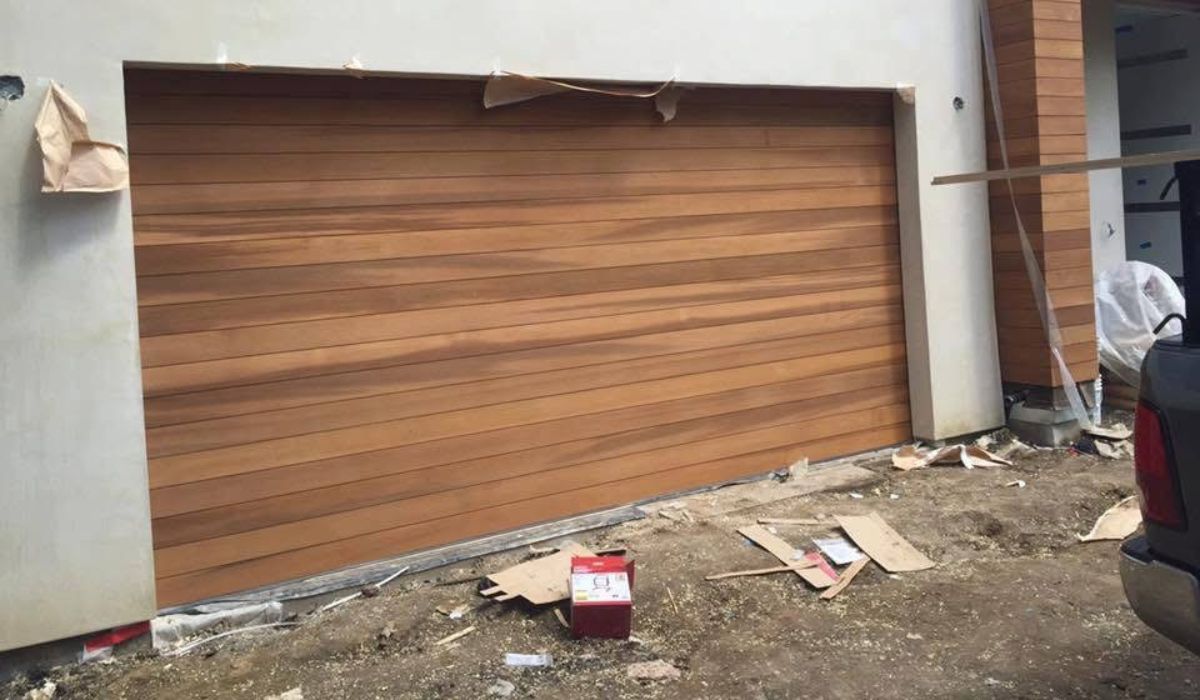 Closed wooden garage door on a house under construction, with debris and a red bucket in front