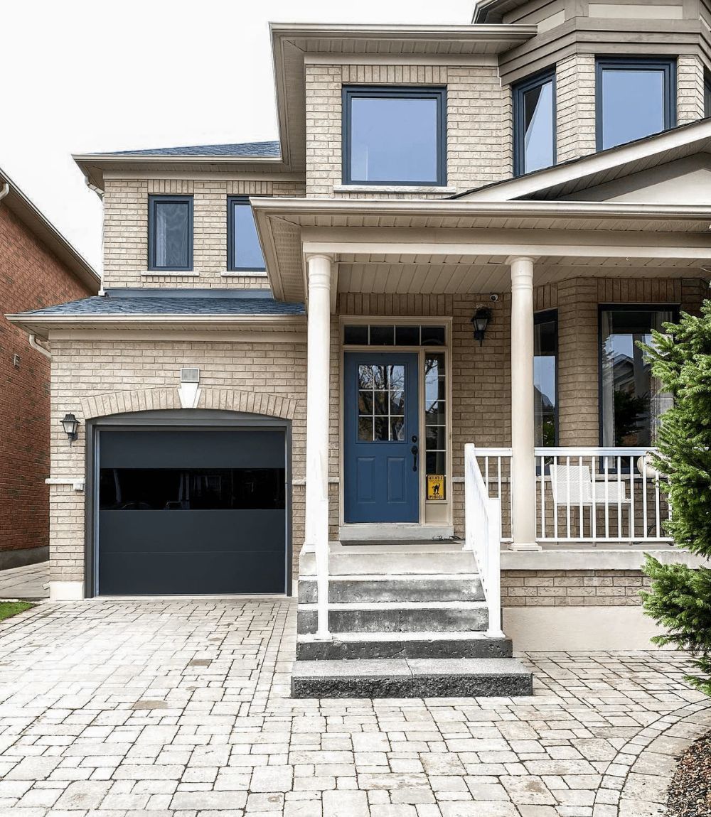 Front view of a beige two-story house with a blue door, black garage, and stone driveway