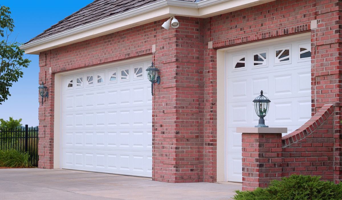 Brick house front with two white garage doors and a lantern on the porch.
