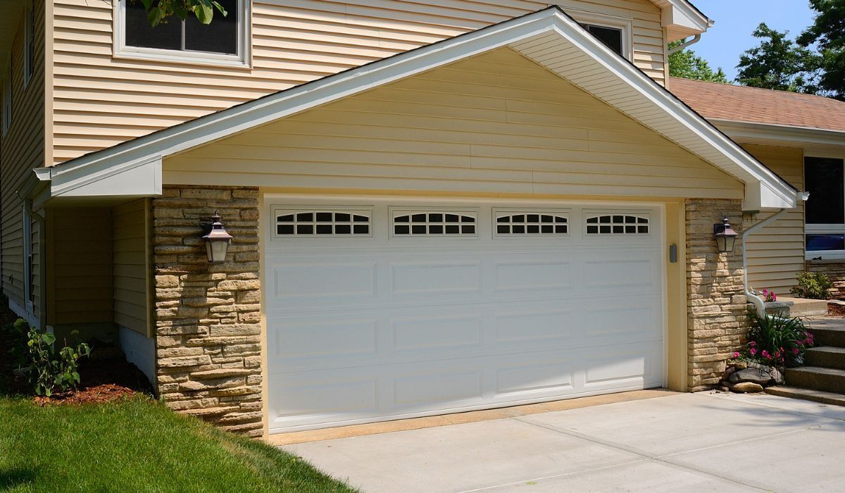 Single-car garage with white door and beige siding on a sunny suburban house