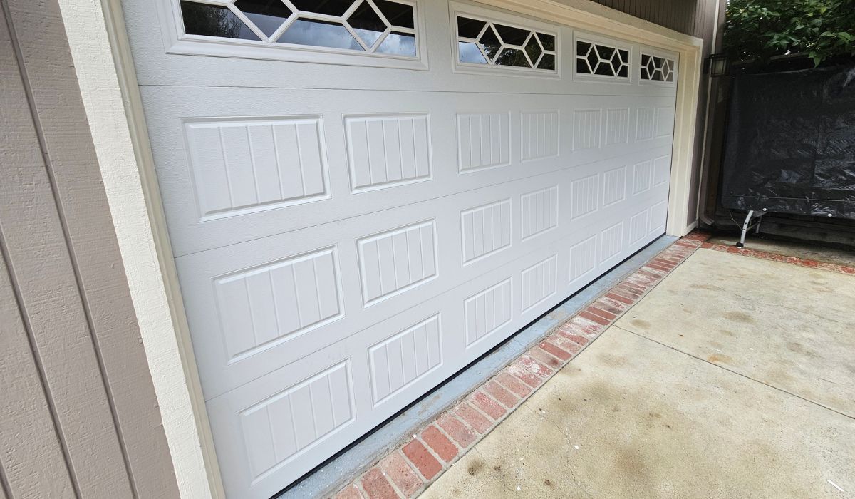 White garage door beside a brick-edged driveway and concrete patio under a covered entry