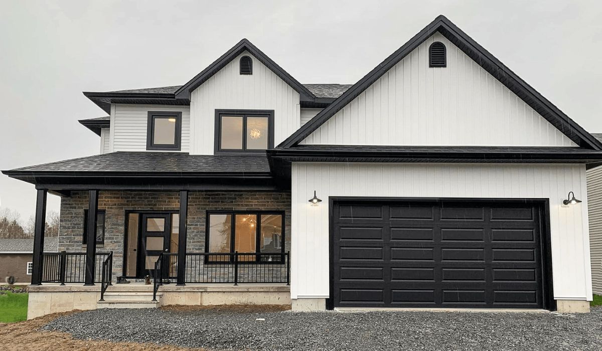 Modern two-story white house with black trim, covered porch, and attached black garage on a gravel lot