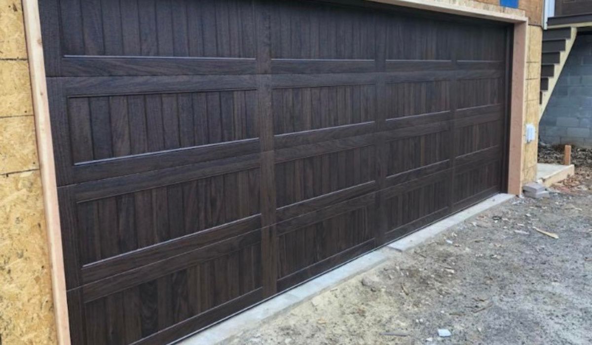 Dark brown wooden garage door on a stone-lined driveway beside a house