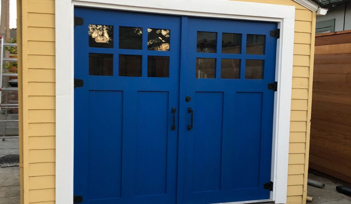 Blue double garage door with small windows on a yellow house exterior