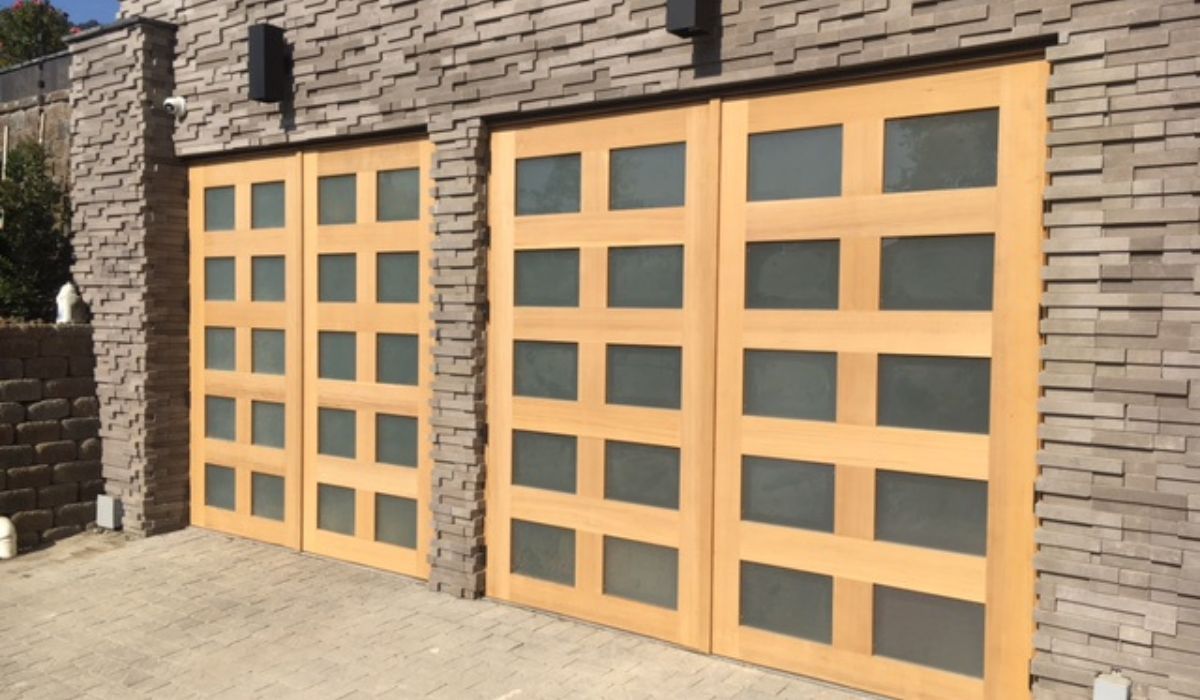 Two tan garage doors with square windows set in a stone wall.