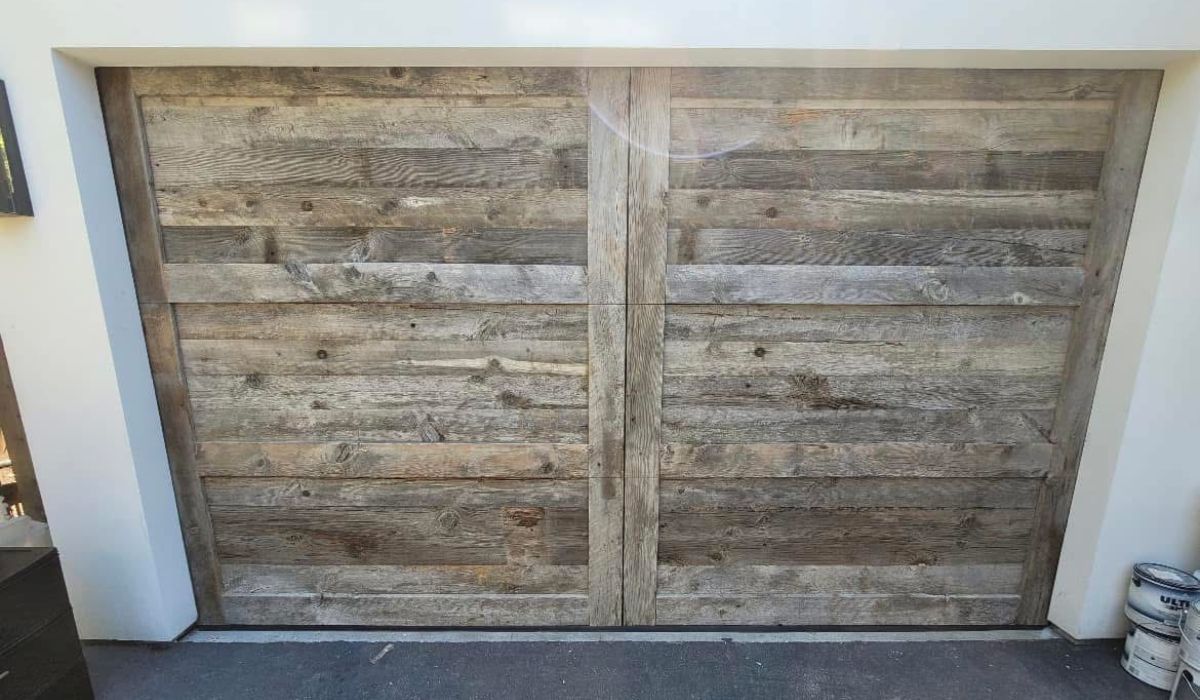 Rustic wooden double gate with weathered gray planks in a white stucco wall opening