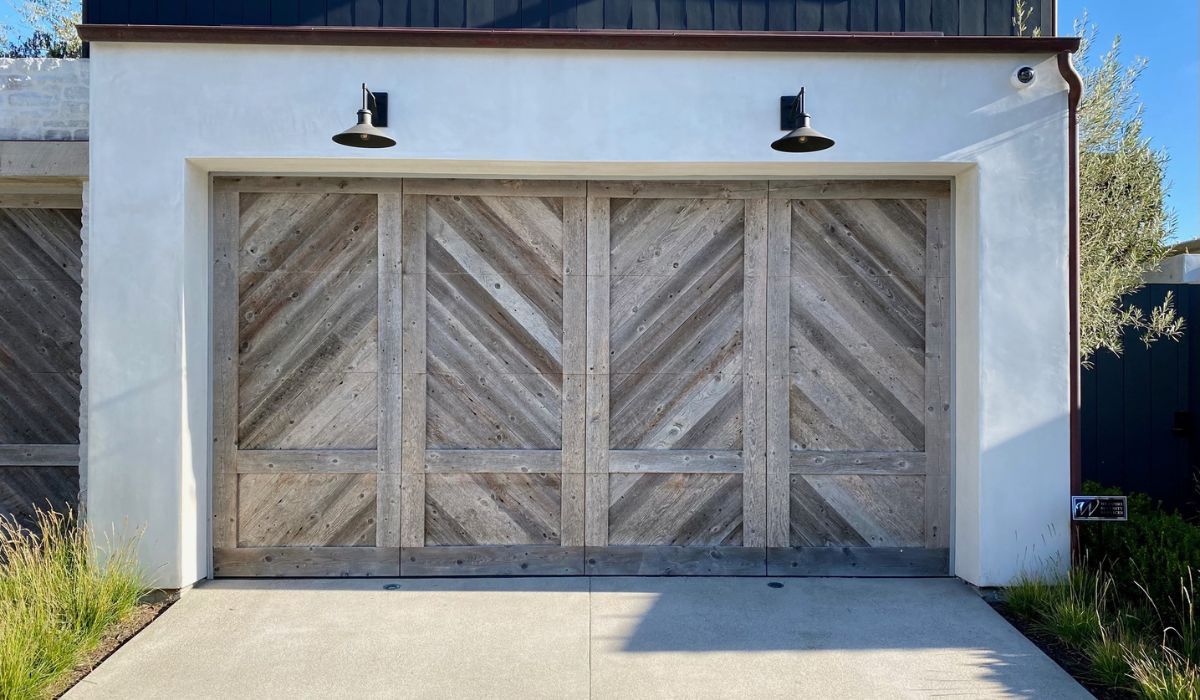 White garage with three wooden doors and black lights above, viewed from the driveway