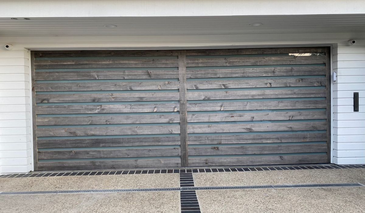 Weathered wooden garage door with two panels and a black handle, set in a white exterior wall.