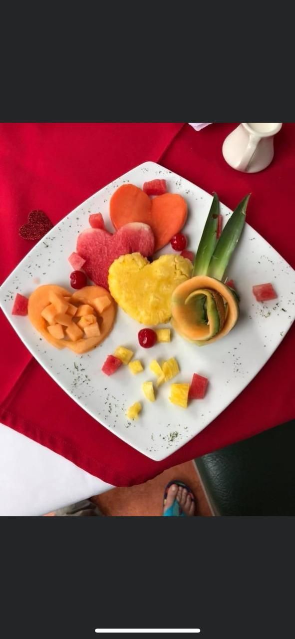 Un plato blanco cubierto de frutas y verduras sobre un mantel rojo.