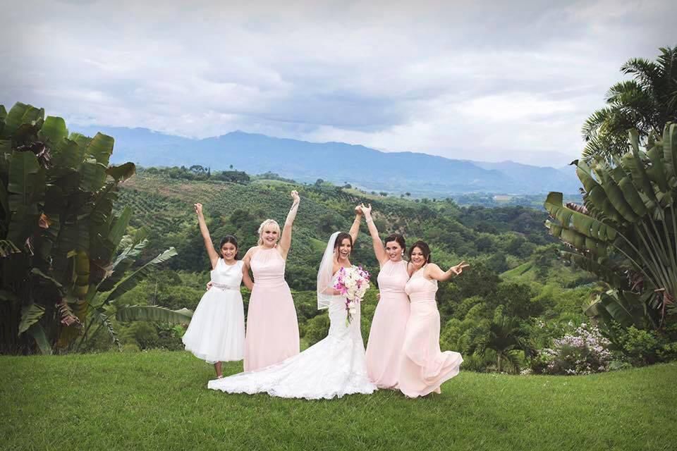 Una novia y sus damas de honor posan para una fotografía en un campo con montañas al fondo.