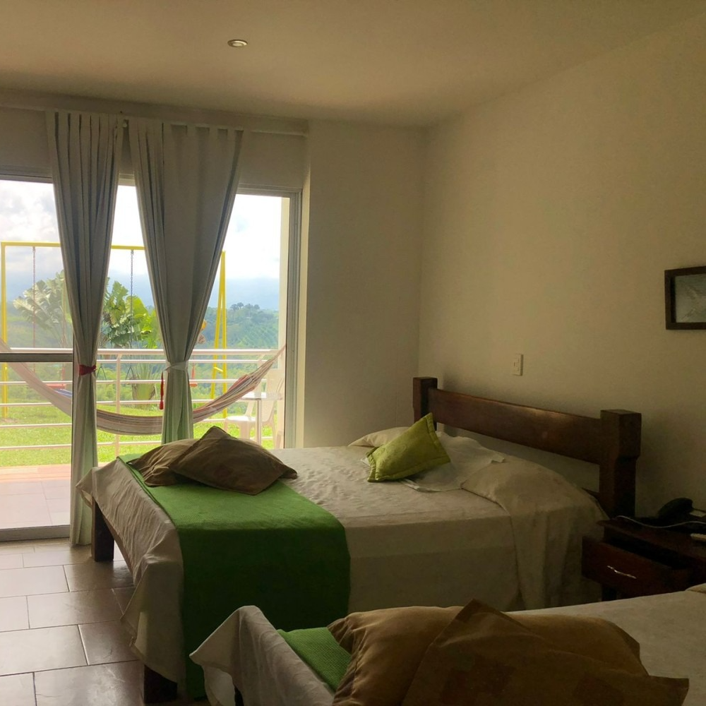 Un dormitorio con dos camas y una hamaca en la ventana.