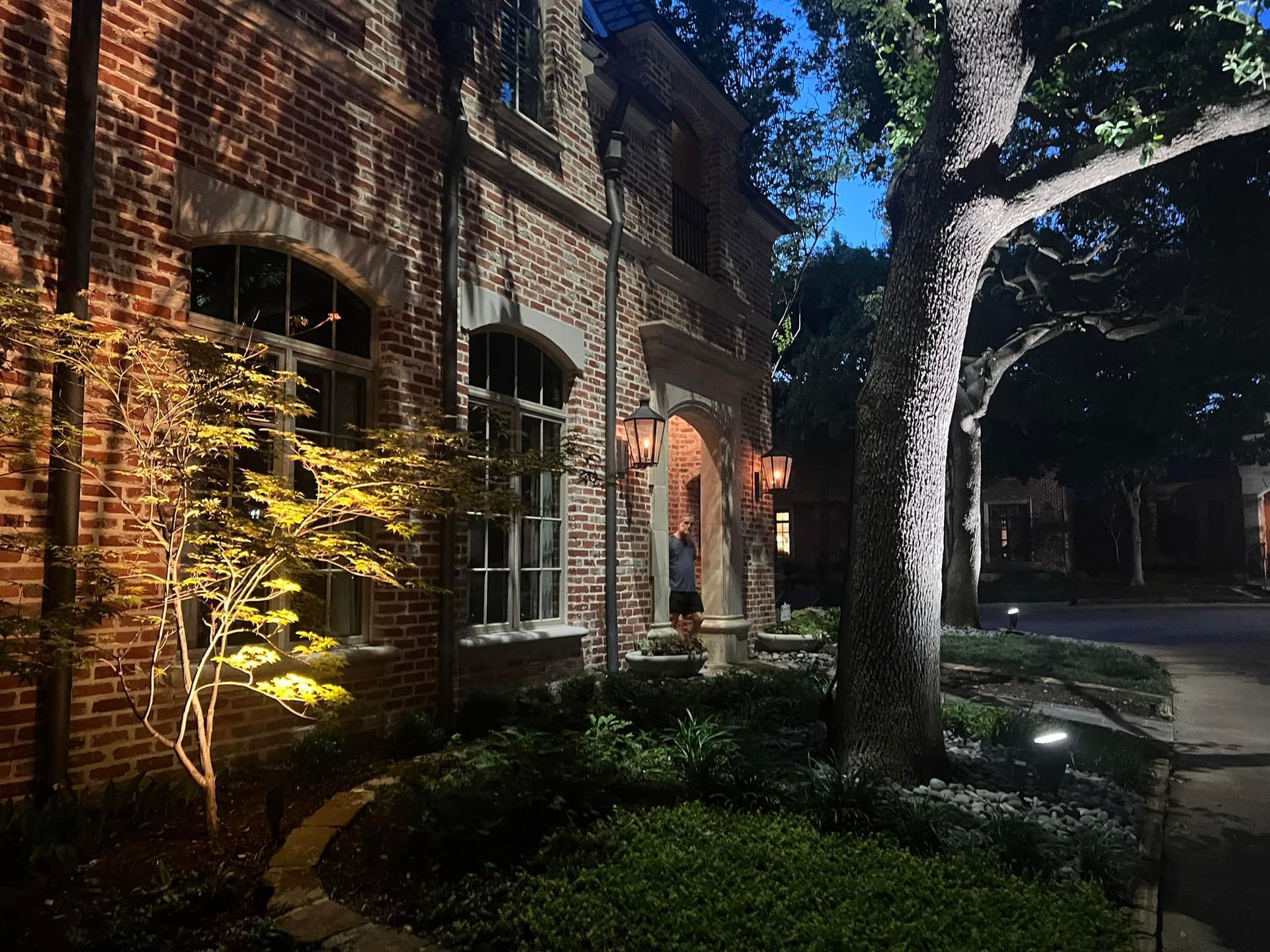 A brick house is lit up at night with trees in front of it.