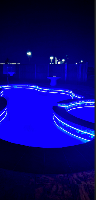 A swimming pool is lit up with blue lights at night