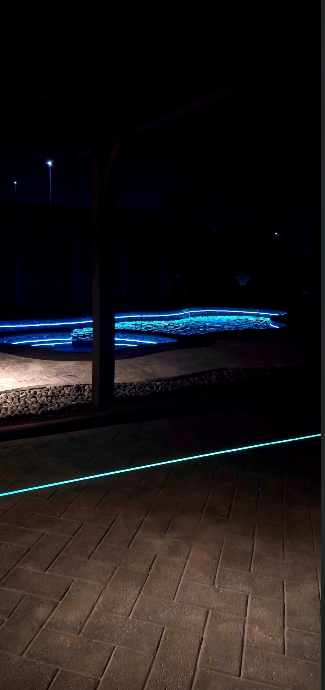 A swimming pool is lit up at night with a blue light coming out of it.