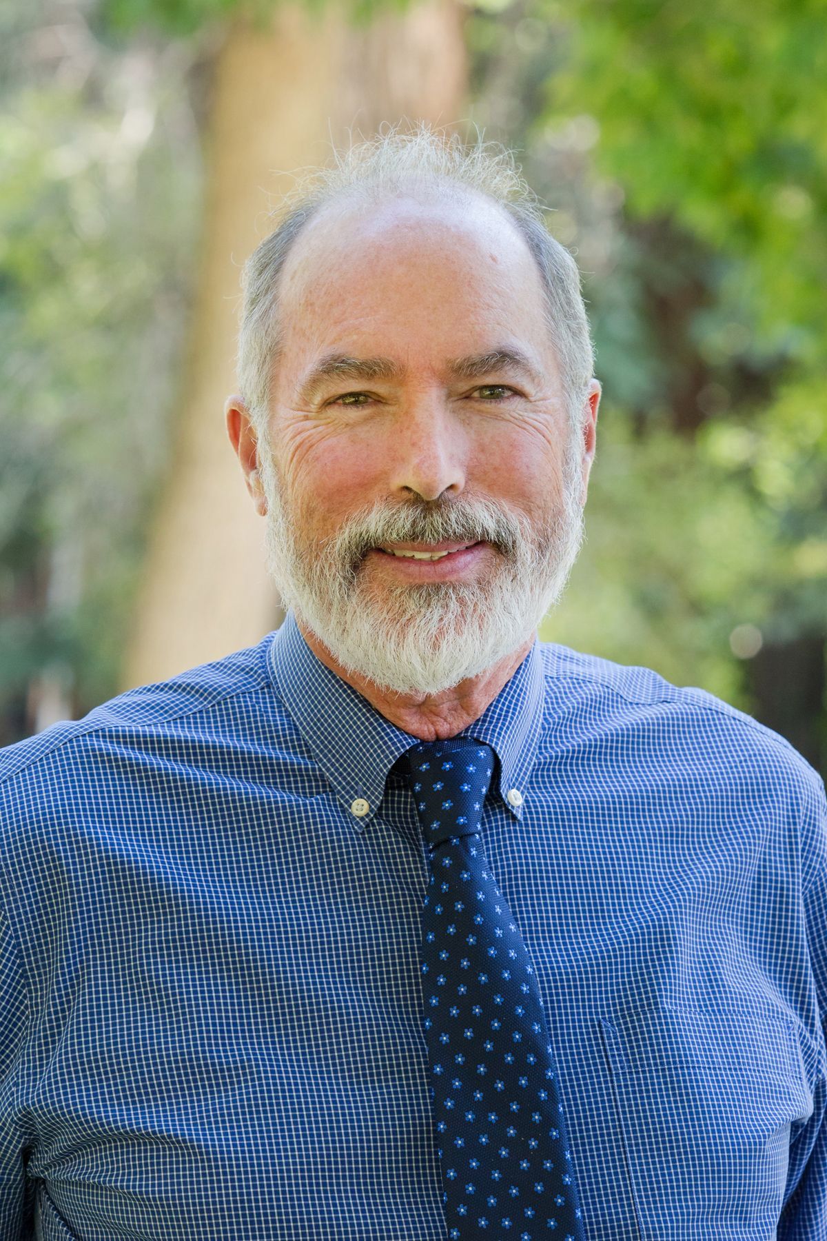 A man with a beard is wearing a blue shirt and tie.