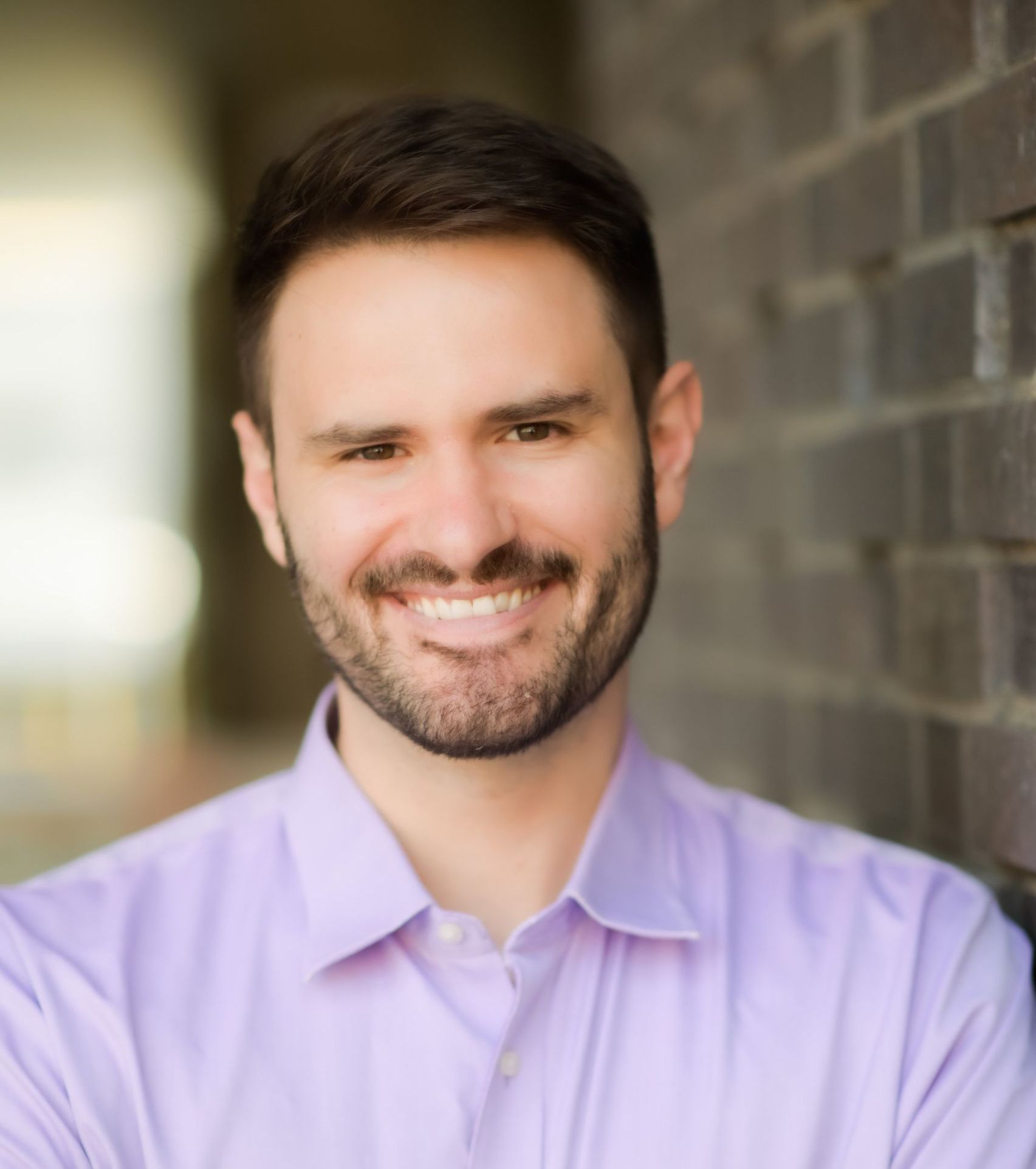 A man with a beard is wearing a blue shirt and smiling.