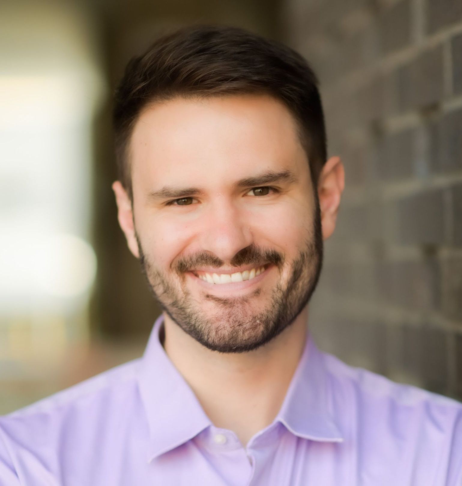 A man with a beard is wearing a blue shirt and smiling.