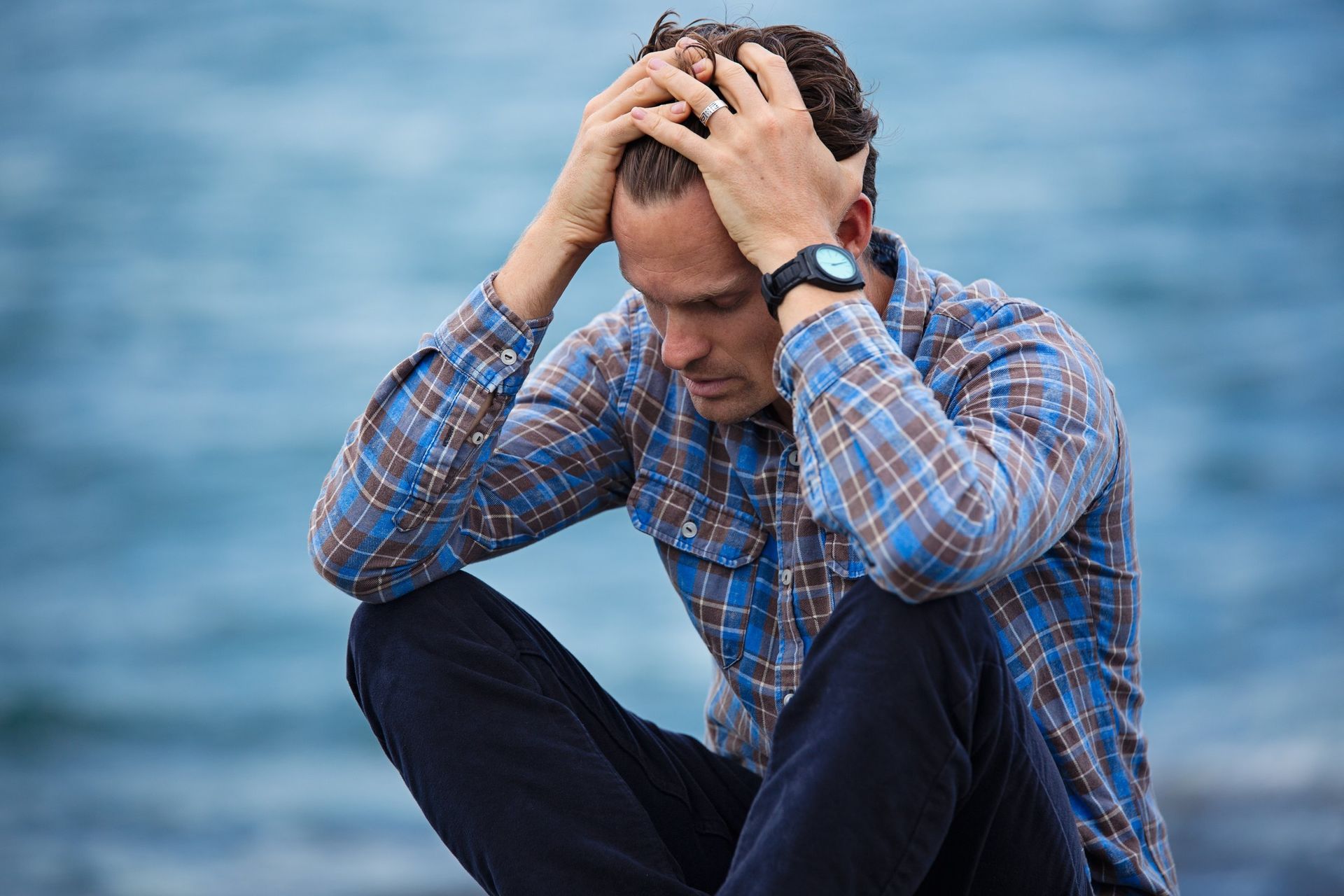 A man is sitting on the beach with his hands on his head.