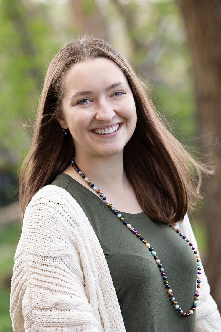 A woman wearing a green shirt and a white sweater is smiling for the camera.