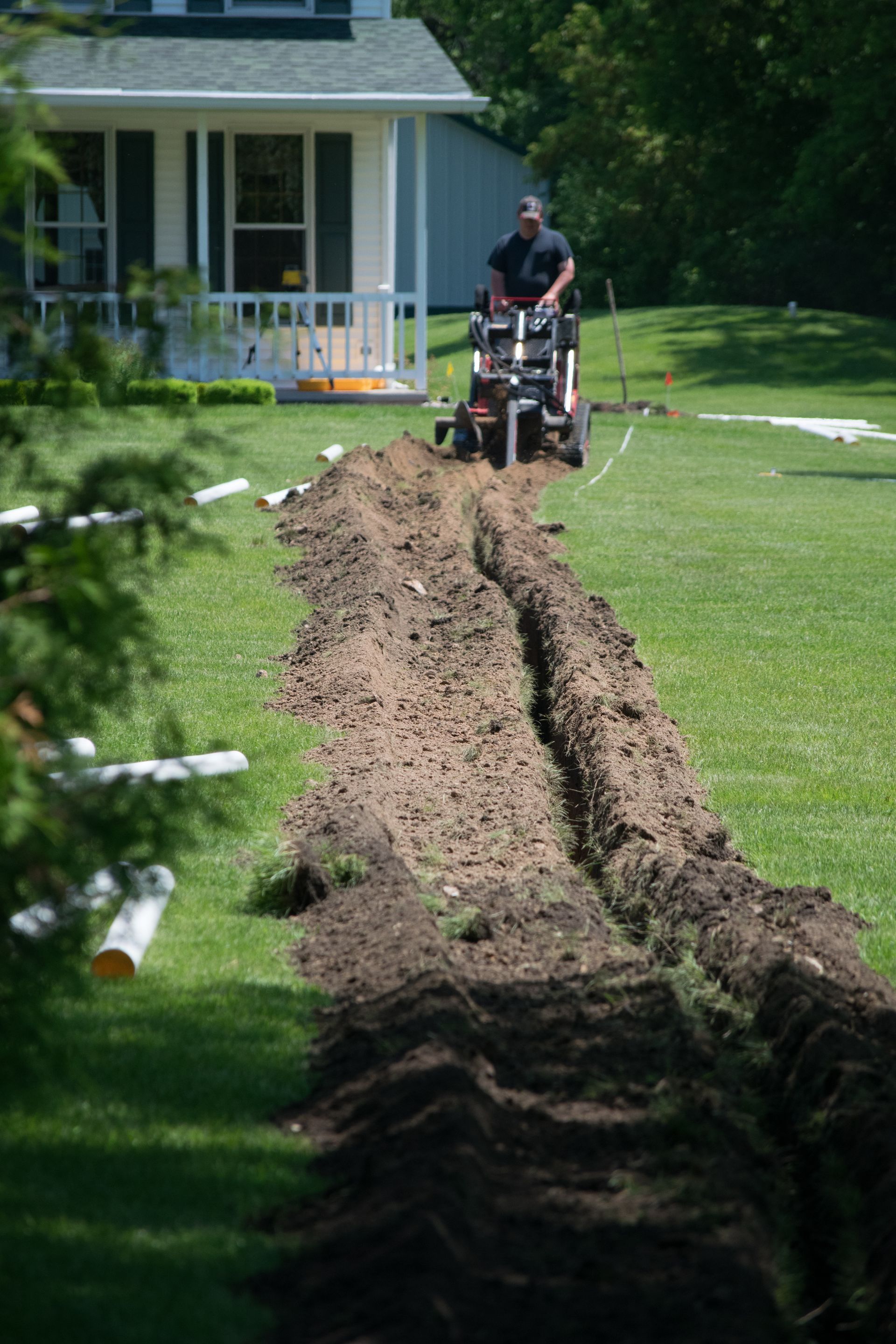 a man is digging a trench in the grass in front of a house .