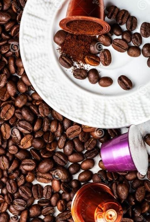 Tres cápsulas de café están encima de una pila de granos de café.