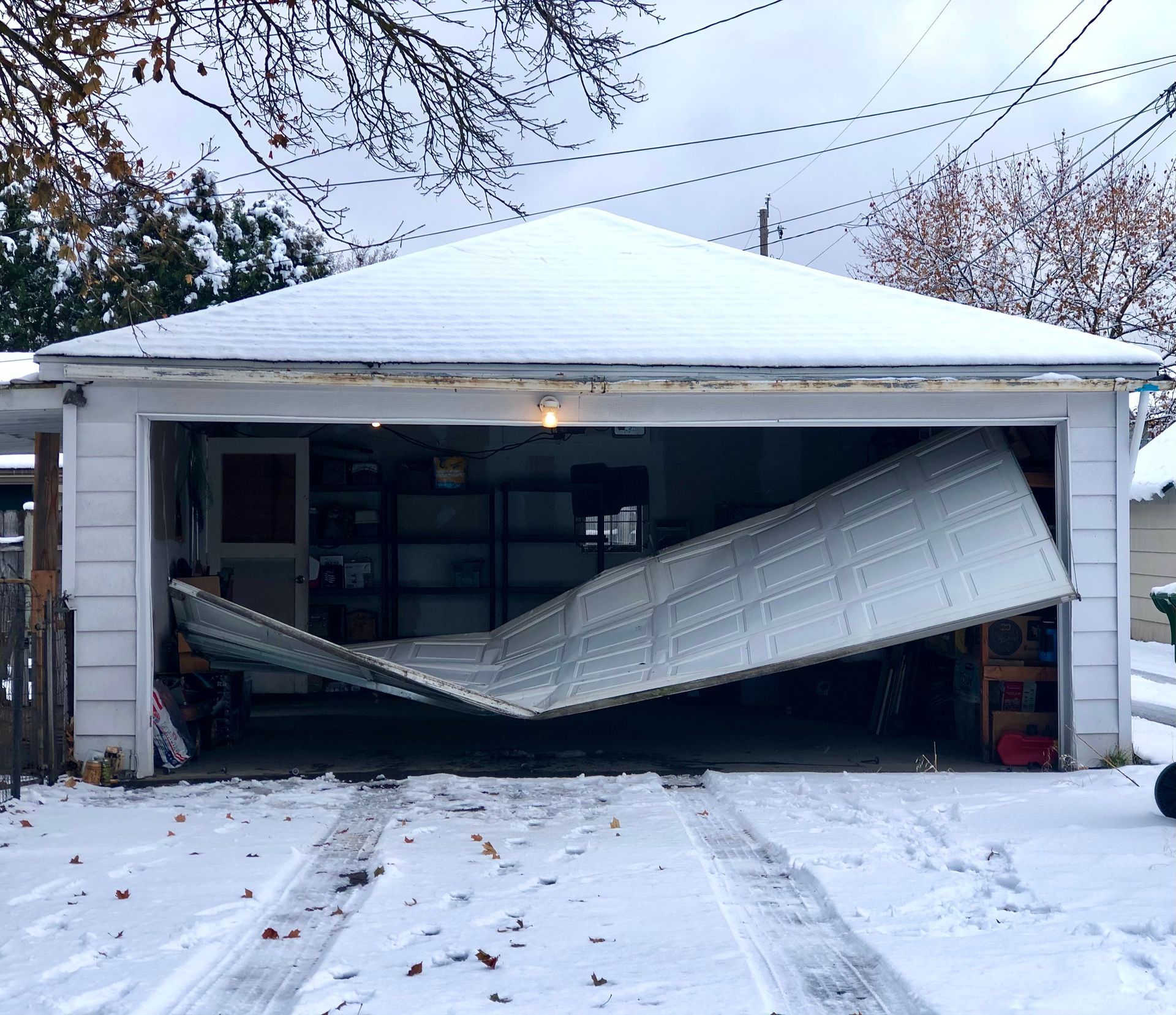 Snow-covered garage with a collapsed overhead door bent inward.
