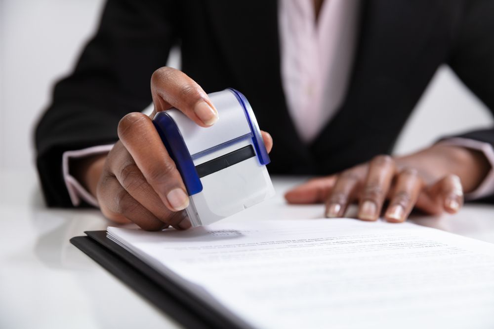 Hands signing a document at a desk during a legal meeting, with a scale and gavel nearby.