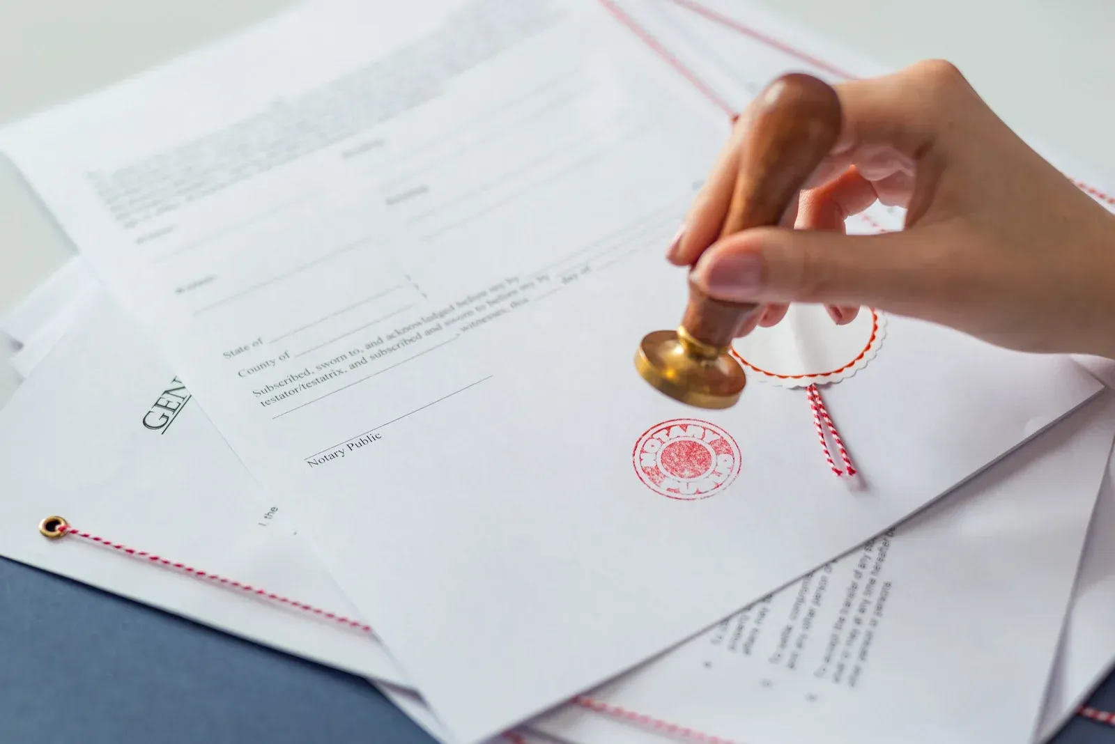 Hand stamping a red seal on a document beside a red string and papers