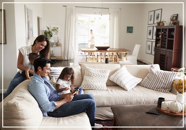 Family relaxing in a light-filled living room. Parents with children on a sofa, one using a tablet.