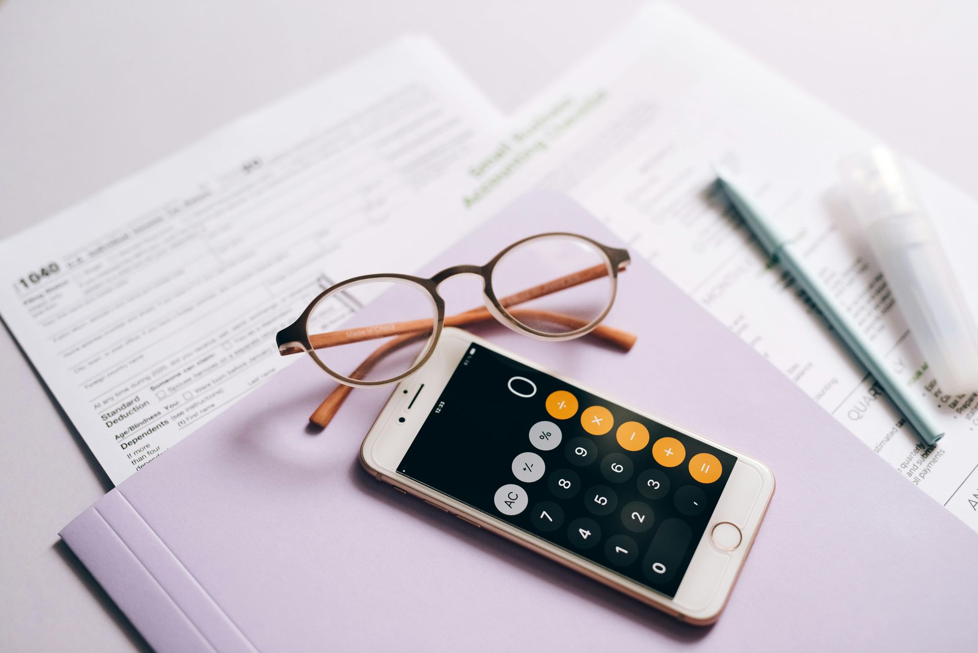 A smartphone with calculator app, eyeglasses, pen, and paperwork on a purple folder.