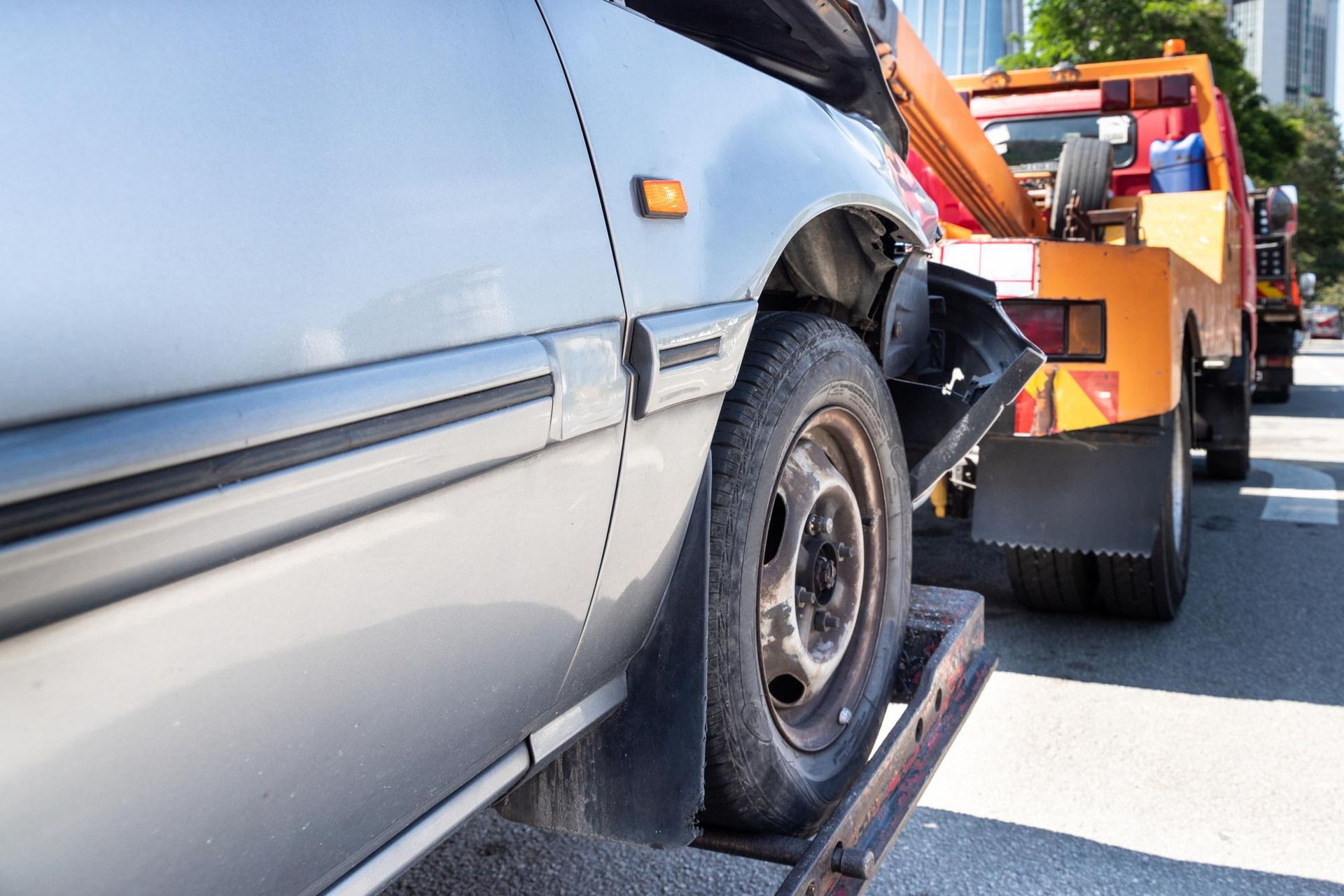 Tow truck loading a gray minivan with a flat tire on a road