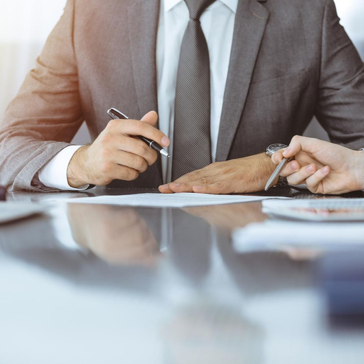 Two people in business attire signing a document at a desk