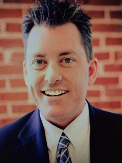 Smiling man in a suit and tie in front of a brick wall
