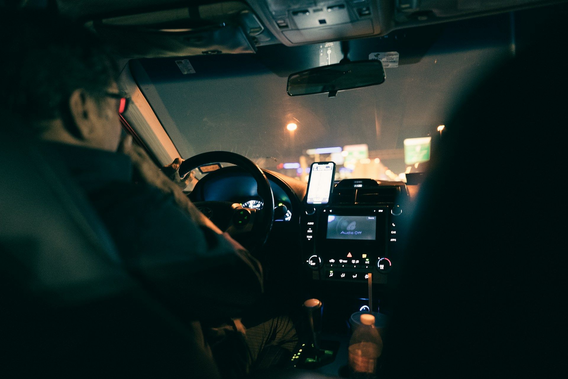 Driver inside a car at night, navigating through city traffic with a lit dashboard and phone mount