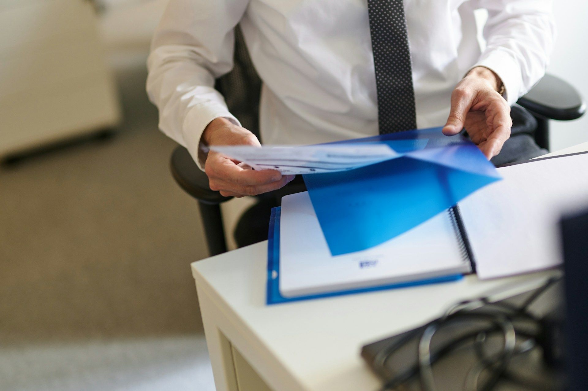 Person in a white shirt reviewing documents at a desk with a blue folder and laptop