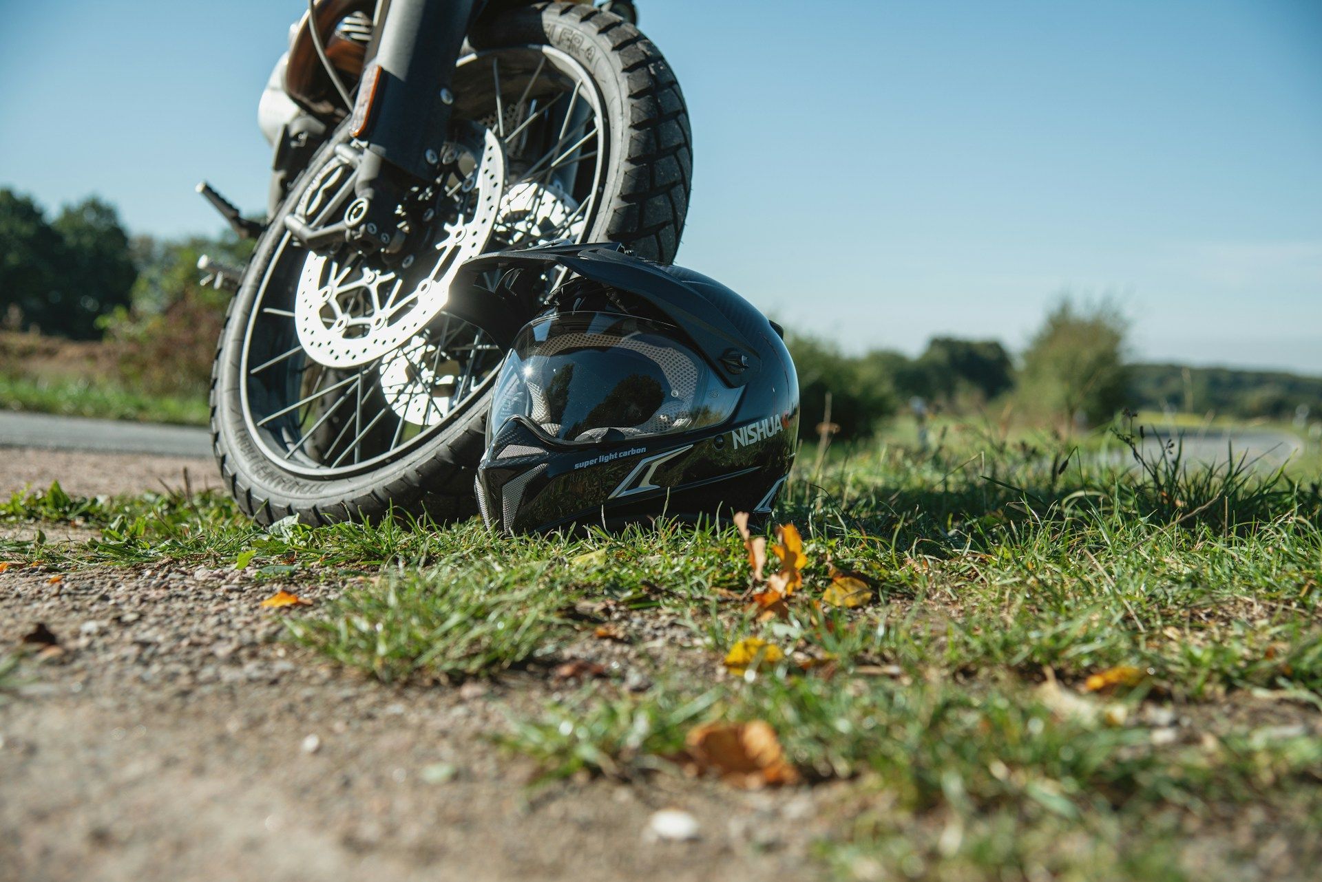 Motorcycle front wheel and helmet on a dirt path, with the bike tipped over in a grassy field