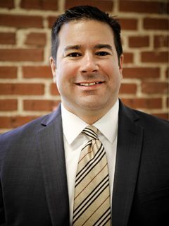 Smiling man in a dark suit and striped tie standing before a brick wall