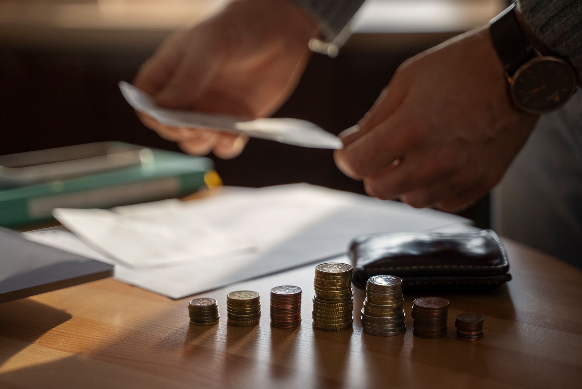 Una persona sostiene un trozo de papel y apila monedas sobre una mesa.
