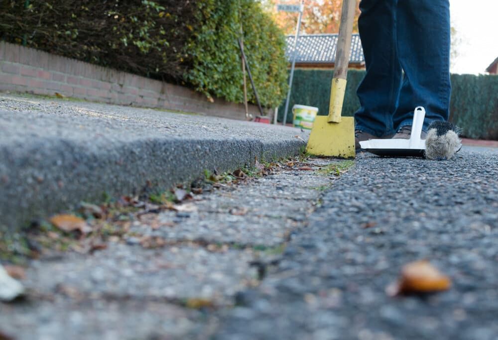 Person Sweeping a Sidewalk Gutter With a Yellow Broom — Cleanaroo Services in Conder, ACT
