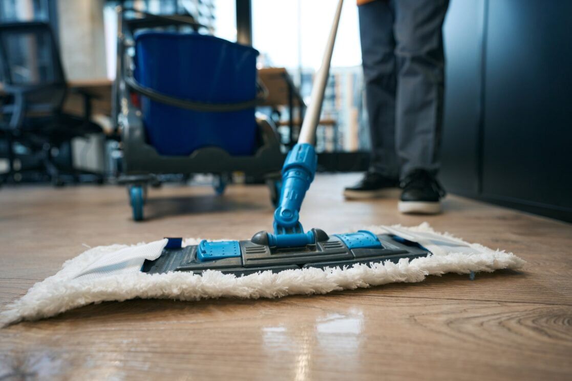 A Person Mopping a Wooden Floor With a Blue Mop — Cleanaroo Services in Conder, ACT