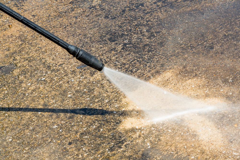 Pressure Washer Spraying a Concrete Surface, Creating a Fan of Water — Cleanaroo Services in Conder, ACT
