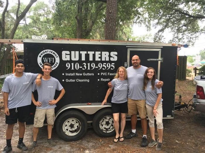 A group of people standing in front of a trailer that says gutters